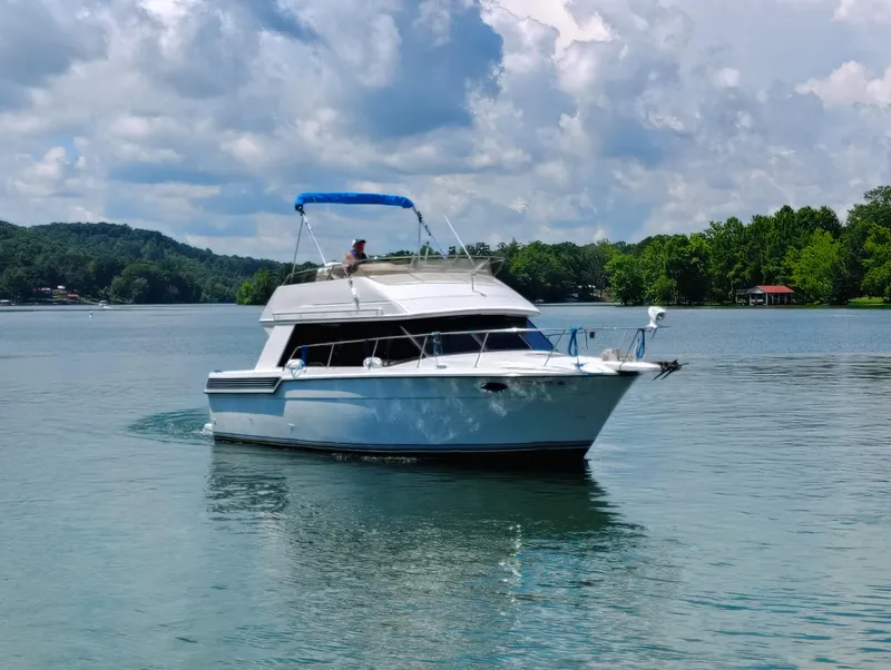 Slide: The Image of 1992 Carver Command Bridge 28 yacht cruising on a serene lake under a partly cloudy sky. - 0