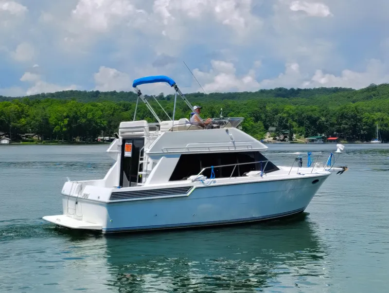 Slide: The Image of 1992 Carver Command Bridge 28 yacht cruising on a serene lake with lush green hills. - 33