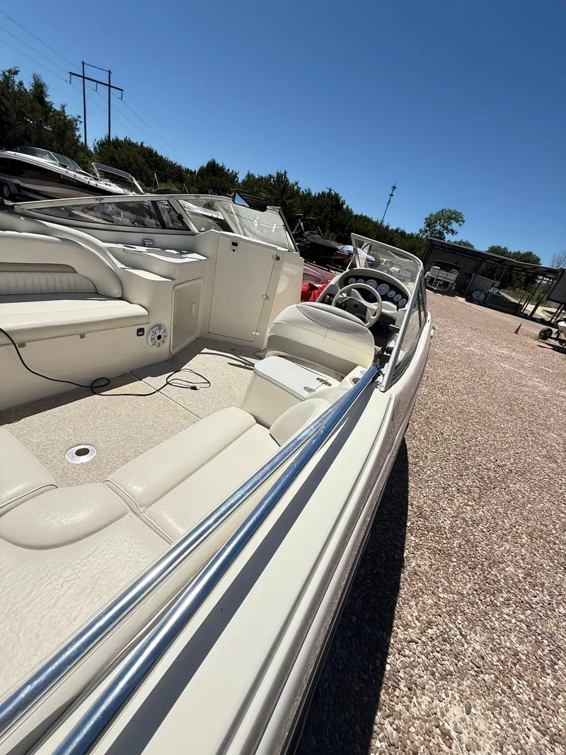 Slide: The Image of 2005 Stingray 220 DR boat interior with white seating and steering wheel, parked outdoors. - 11