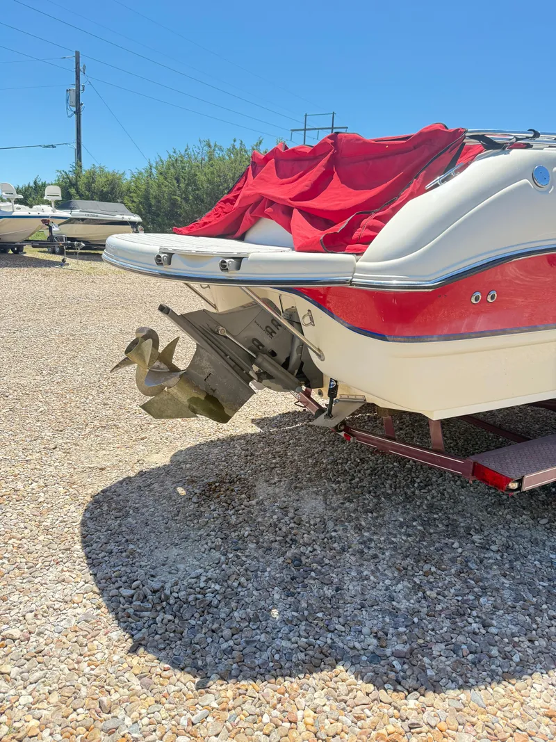 Slide: The Image of 2005 Stingray 220 DR boat with red cover, parked on gravel under clear blue sky. - 4