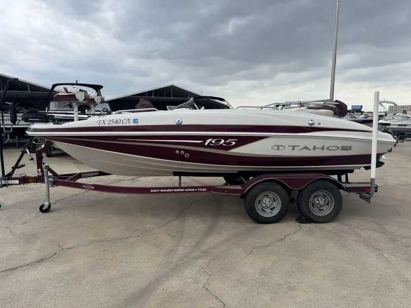 Slide: The Image of 2013 Tahoe 195 boat on trailer, maroon and white, parked outdoors. - 0