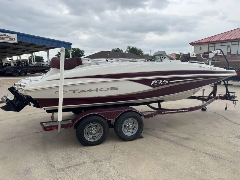 Slide: The Image of 2013 Tahoe 195 boat on trailer, parked outdoors under cloudy sky. - 2