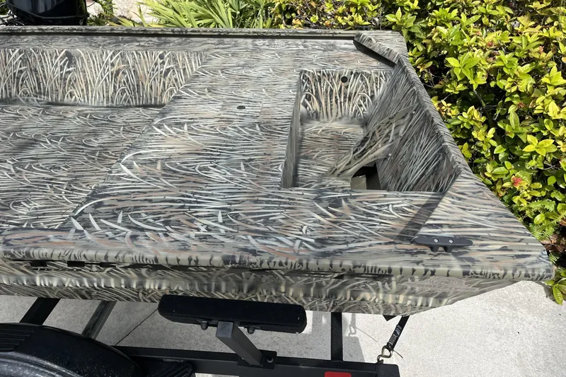 Slide: The Image of 2025 Tracker Grizzly 1860 Utility boat with camouflage pattern, parked near greenery. - 3