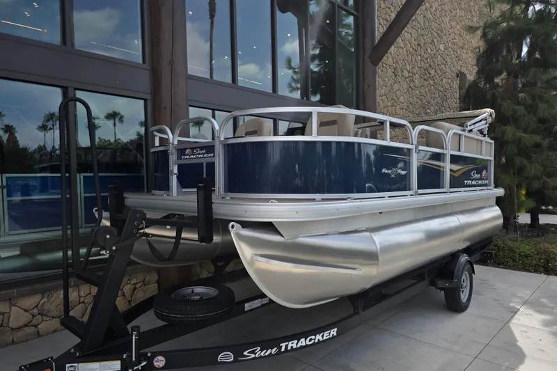 Slide: The Image of 2025 Sun Tracker Bass Buggy 16 XL Select pontoon boat on trailer, outdoor display. - 1