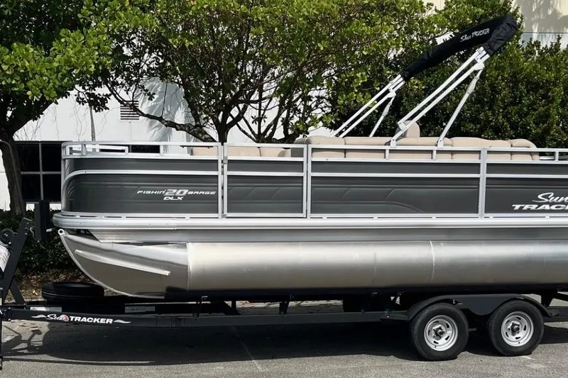 The Image of 2025 Sun Tracker Fishin' Barge 20 DLX pontoon boat on trailer, parked outdoors. - 0