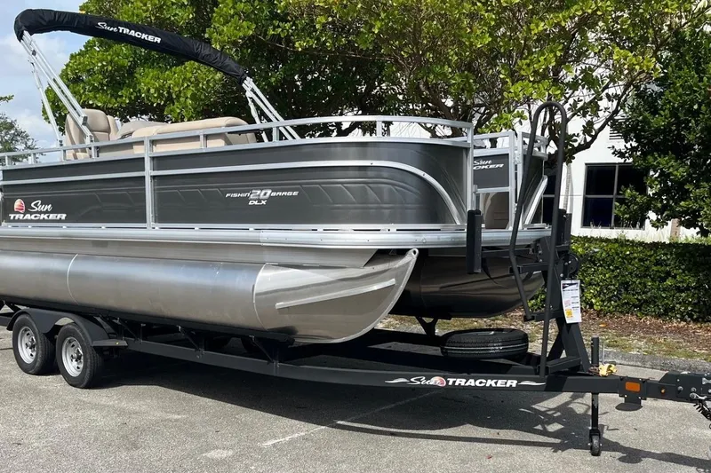 Slide: The Image of 2025 Sun Tracker Fishin' Barge 20 DLX pontoon boat on trailer, parked outdoors. - 2
