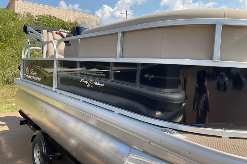 Slide: The Image of 2025 Sun Tracker Bass Buggy 16 XL Select pontoon boat, side view, parked outdoors. - 72