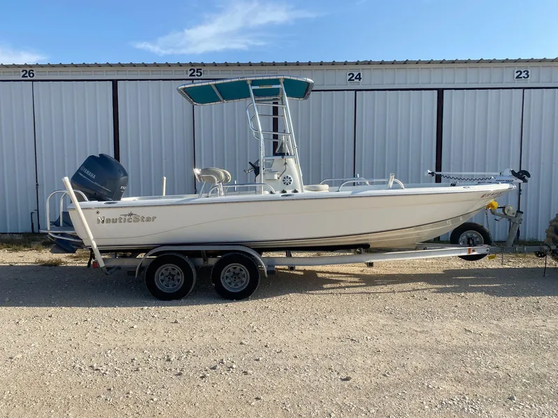 Slide: The Image of 2015 NauticStar 2200 Sport boat on trailer, parked outdoors near storage units. - 0