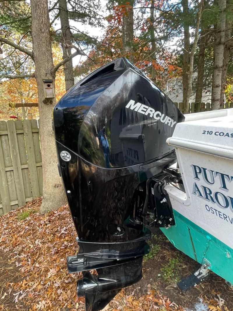 Slide: The Image of 1998 Wellcraft 210 Coastal boat with Mercury outboard motor, parked near trees and a wooden fence. - 5