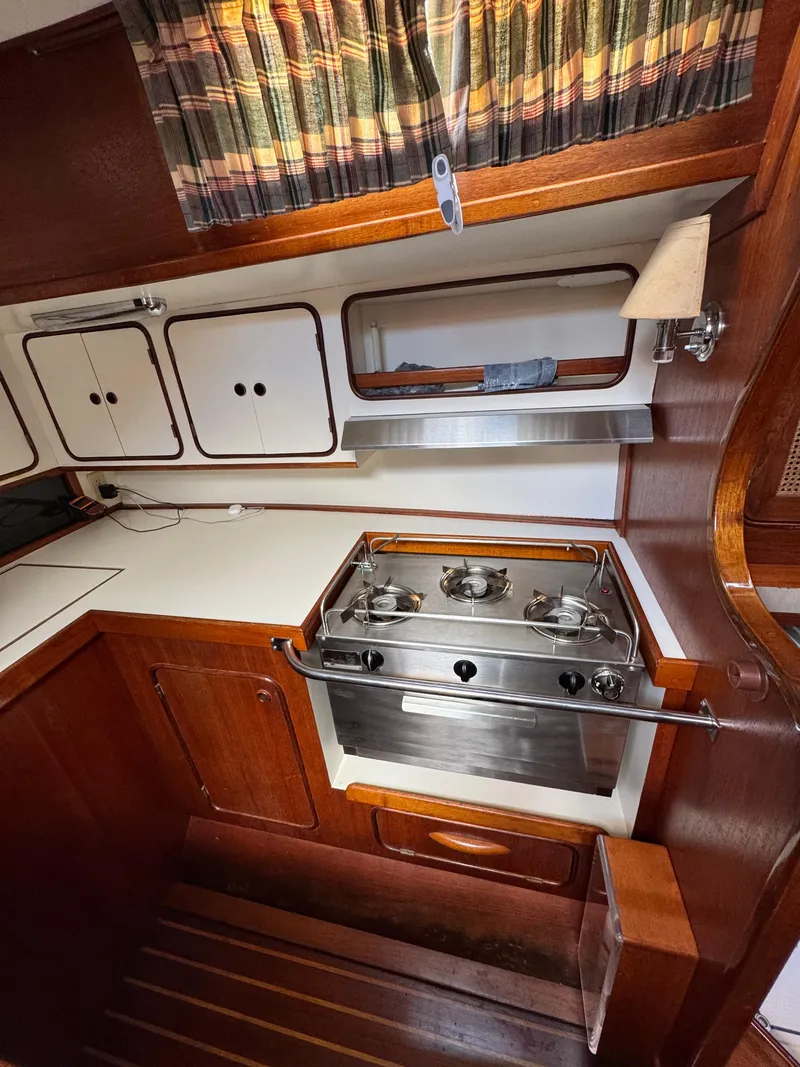 Slide: The Image of 1981 Gulfstar 44 yacht kitchen with stove, wooden cabinets, and striped curtains. - 27