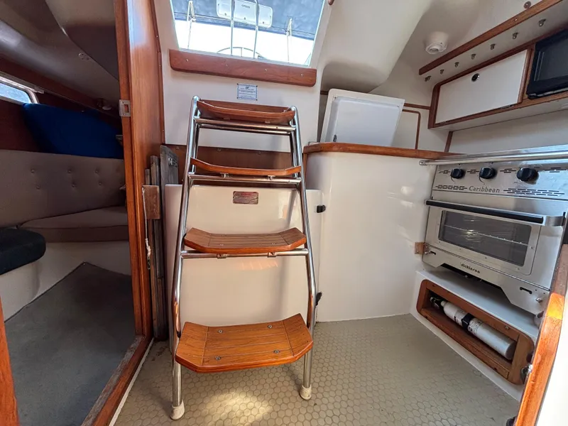 Slide: The Image of Interior of a 1998 Catalina 320 sailboat with wooden steps and a compact kitchen area. - 18