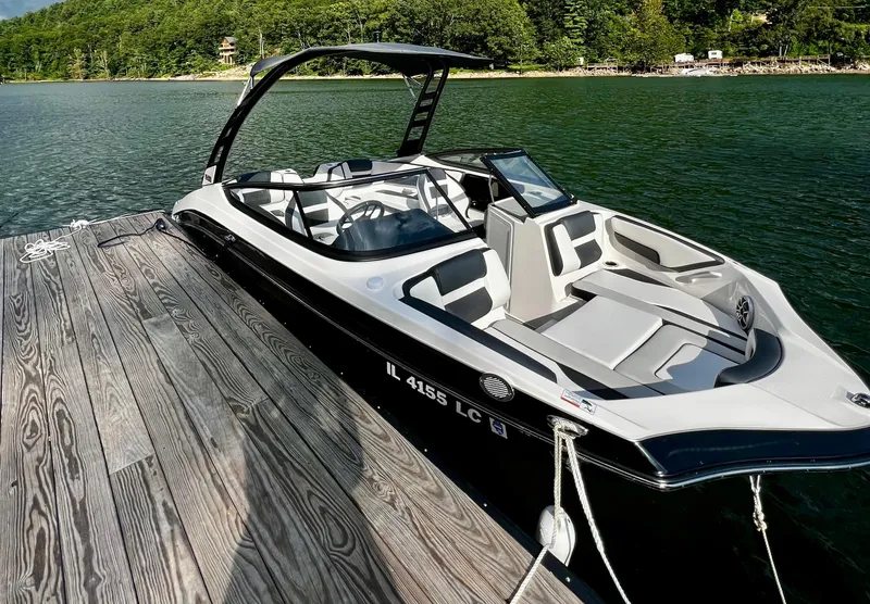 The Image of 2022 Yamaha Boats 195 S docked on a serene lake with lush green surroundings. - 1