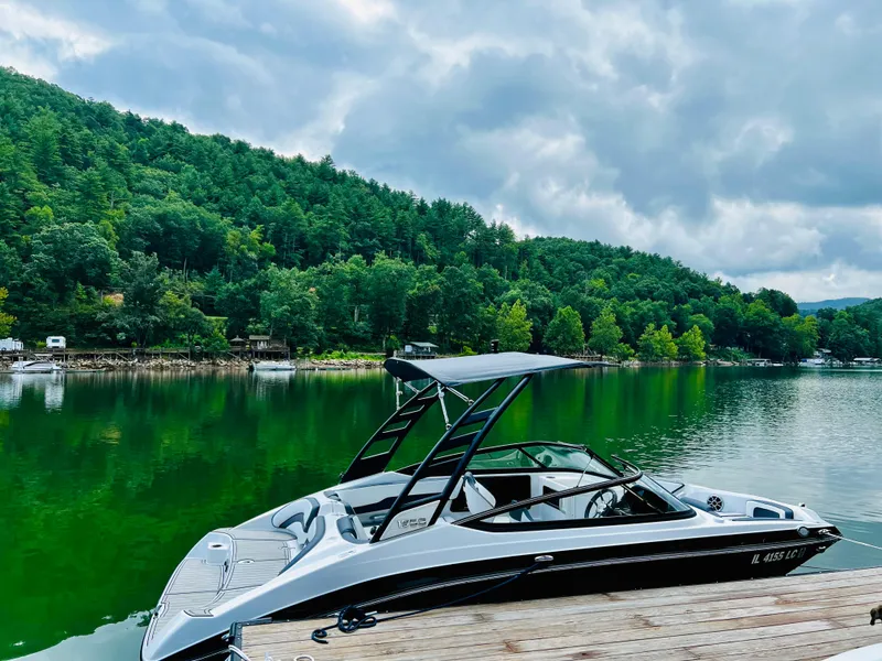 Slide: The Image of 2022 Yamaha Boats 195 S docked on a serene lake with lush green hills. - 5