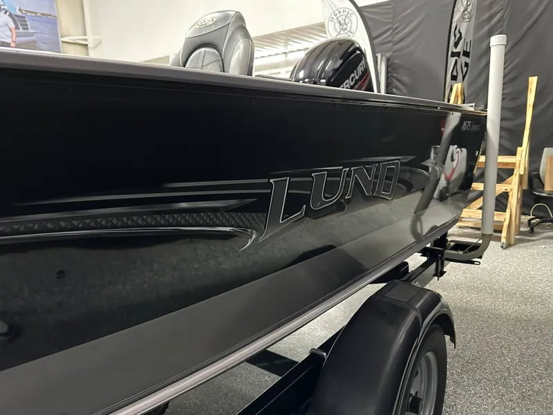 Slide: The Image of 2017 Lund 1675 Impact SS boat, black exterior, displayed indoors on a trailer. - 4