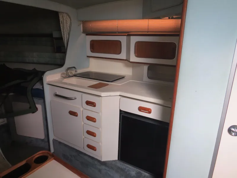 Slide: The Image of 1989 Sea Ray Sundancer 280 interior kitchen with cabinets, sink, and compact fridge. - 13
