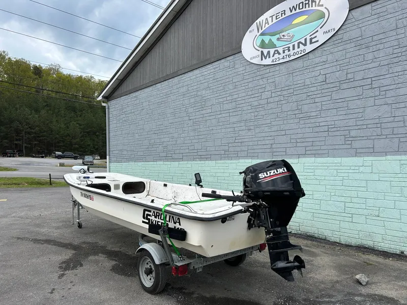 Slide: The Image of 2004 Carolina Skiff J1650 boat with Suzuki motor on trailer, parked outside marine shop. - 3