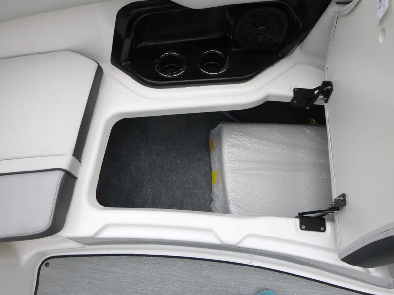 Slide: The Image of 2025 Yamaha Boats AR250 storage compartment with open hatch and cup holders. - 13