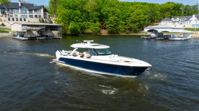 Slide: The Image of 2024 Tiara Yachts 43 LS cruising on a scenic lake with docks and greenery. - 0