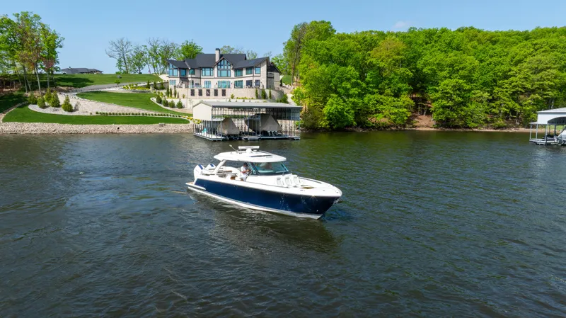 Slide: The Image of 2024 Tiara Yachts 43 LS cruising on a scenic lake near a luxurious waterfront home. - 16