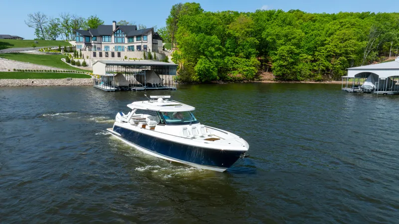 Slide: The Image of 2024 Tiara Yachts 43 LS cruising on a scenic lake near luxury waterfront homes. - 17