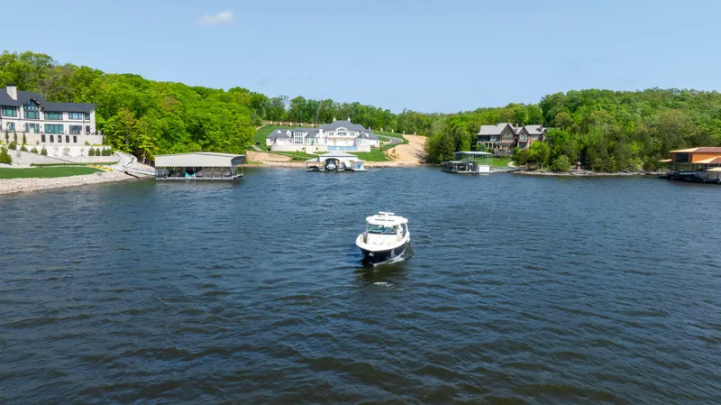 Slide: The Image of 2024 Tiara Yachts 43 LS cruising on a scenic lake with waterfront homes. - 22