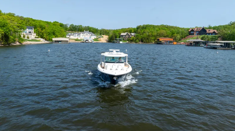 Slide: The Image of 2024 Tiara Yachts 43 LS cruising on a scenic lake with lush green surroundings. - 23