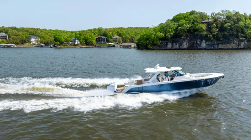 Slide: The Image of 2024 Tiara Yachts 43 LS cruising on a scenic lake with lush green shoreline. - 26