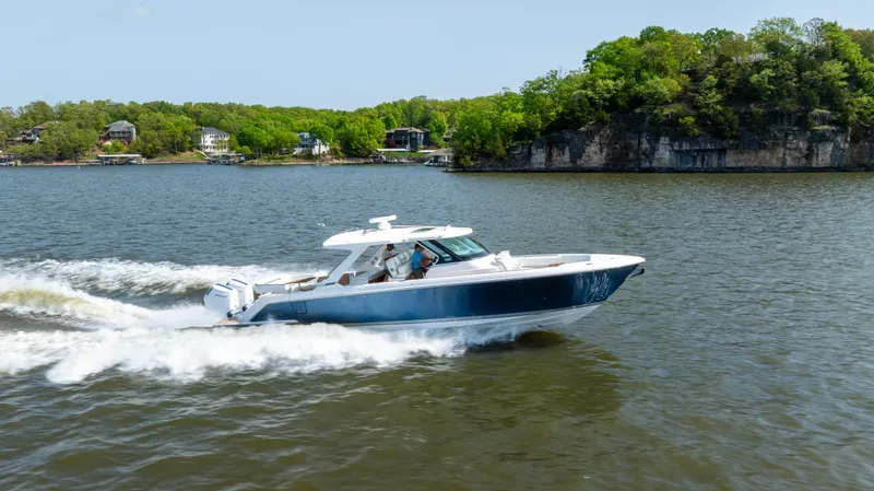 Slide: The Image of 2024 Tiara Yachts 43 LS cruising on a scenic lake with lush green shoreline. - 27