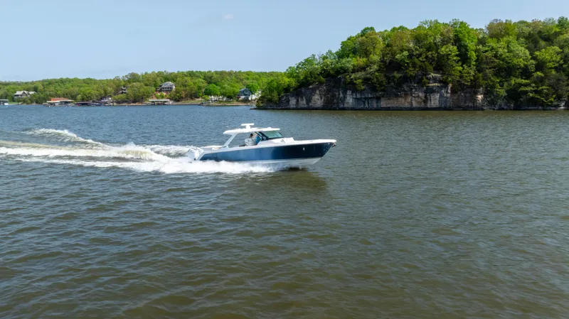 Slide: The Image of 2024 Tiara Yachts 43 LS cruising on a scenic lake with lush green shoreline. - 28