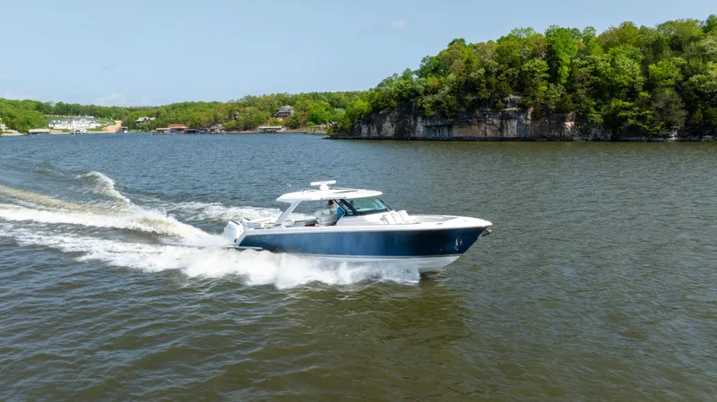 Slide: The Image of 2024 Tiara Yachts 43 LS cruising on a scenic lake with lush green shoreline. - 29