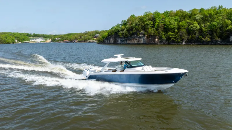 Slide: The Image of 2024 Tiara Yachts 43 LS cruising on a scenic lake with lush green shoreline. - 30