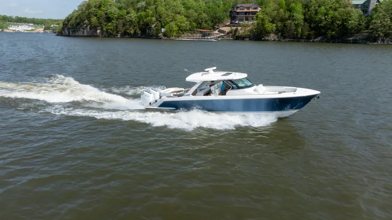 Slide: The Image of 2024 Tiara Yachts 43 LS cruising on a scenic lake with lush green shoreline. - 31