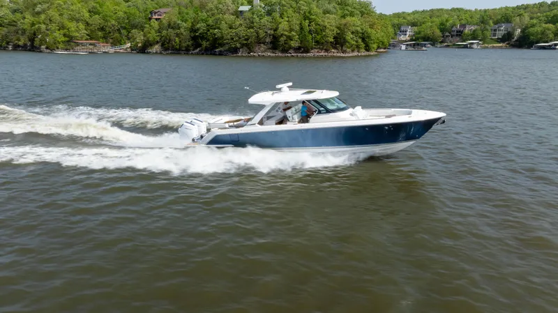 Slide: The Image of 2024 Tiara Yachts 43 LS cruising on a lake with lush green shoreline. - 32