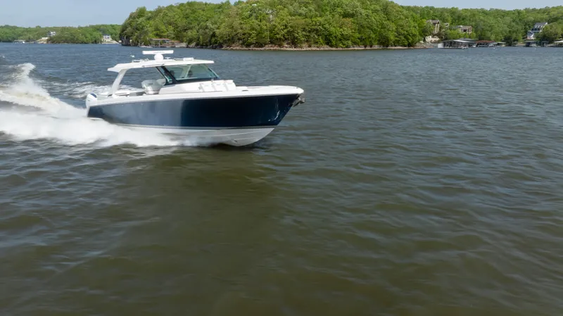 Slide: The Image of 2024 Tiara Yachts 43 LS cruising on a scenic lake with lush green shoreline. - 33