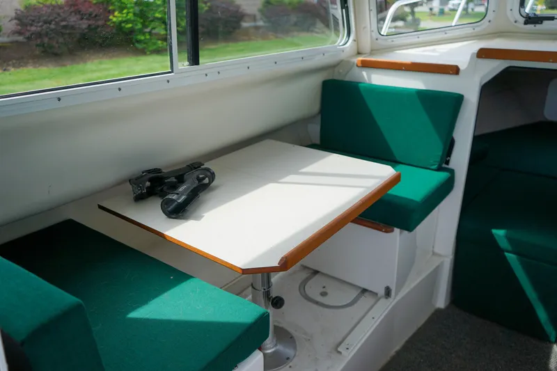 Slide: The Image of 2021 C-Dory 25' Cruiser interior with green seating and a compact dining table. - 18