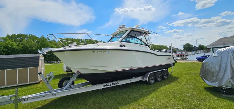 Slide: The Image of 2016 Boston Whaler 285 Conquest boat on trailer, parked on grass under a blue sky. - 2