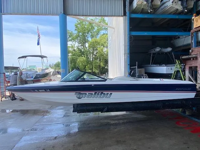 Slide: The Image of 1998 Malibu Response boat in a marina, partially sheltered, with trees and other boats nearby. - 3