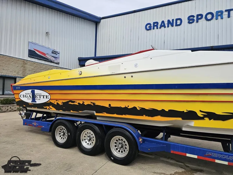 Slide: The Image of 2001 Cigarette 42 Tiger boat with vibrant yellow and orange design on a trailer outside Grand Sport Center. - 7