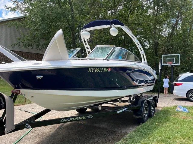 Slide: The Image of 2020 Chaparral 21 Surf boat on trailer in driveway, surrounded by trees and vehicles. - 4
