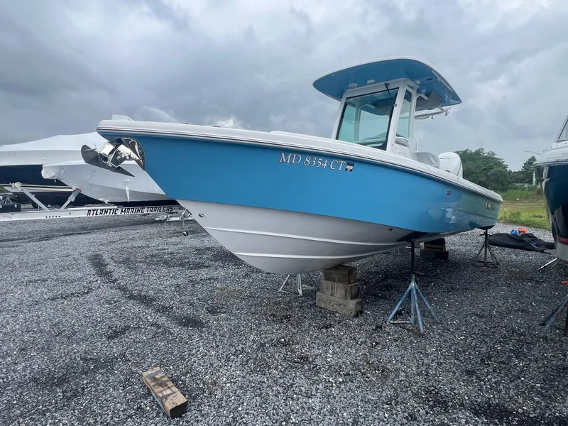 Slide: The Image of 2023 Everglades 253 CC boat on stands, blue hull, overcast sky. - 16