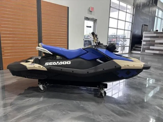 Slide: The Image of 2025 Sea-Doo Spark Trixx Waverunner in showroom, blue and beige design, side view. - 1