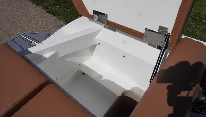 Slide: The Image of 2024 Cobalt CS23 boat storage compartment with open lid, featuring brown seating and white interior. - 14