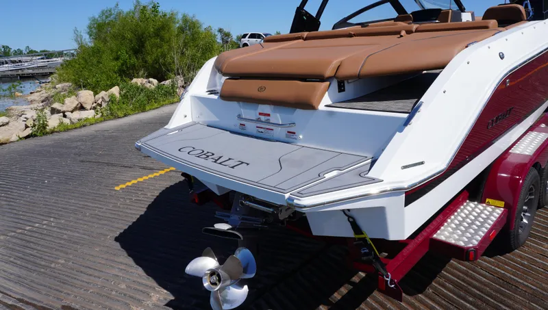 Slide: The Image of 2024 Cobalt CS23 boat on trailer, rear view, near water and greenery. - 3