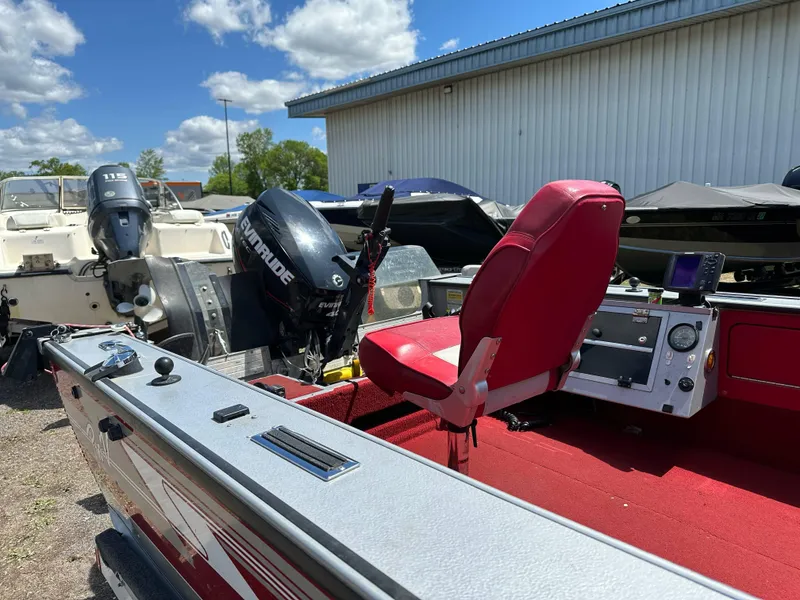 Slide: The Image of 1995 Lund 1660 Pro V Tiller boat with red interior and outboard motor, parked outdoors. - 12