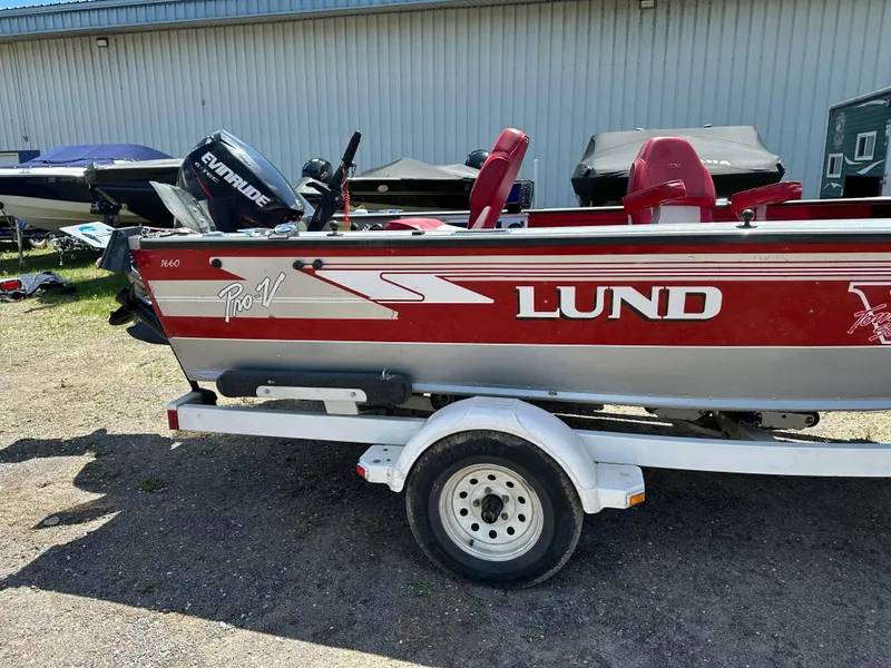 Slide: The Image of 1995 Lund 1660 Pro V Tiller boat on trailer, red and white design, outdoor setting. - 4