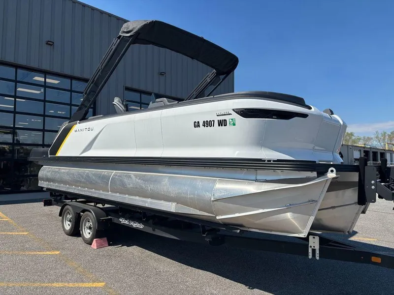 Slide: The Image of 2023 Manitou Explore 22 Max Bench pontoon boat on trailer, parked outdoors. - 23