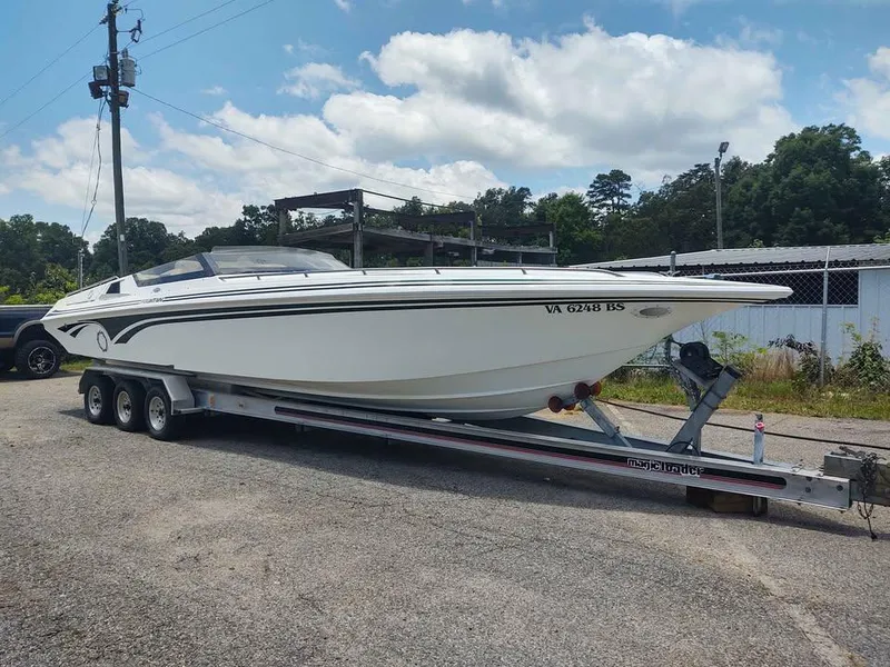 The Image of 1996 Fountain 32 Fever speedboat on trailer, parked outdoors under a partly cloudy sky. - 0
