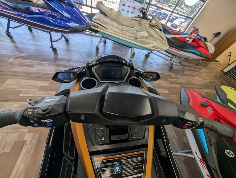 Slide: The Image of 2025 Yamaha FX Cruiser HO with Audio, dashboard view in showroom, surrounded by other jet skis. - 12