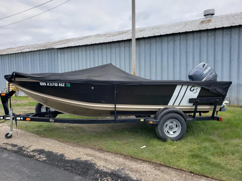 Slide: The Image of 2013 G3 V172C boat on trailer with cover, parked beside a metal building. - 0
