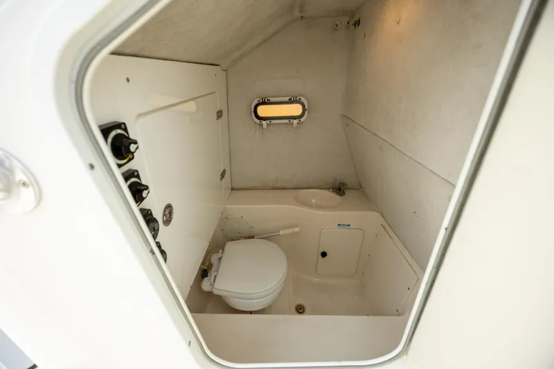 Slide: The Image of 2000 Pursuit 2470 Center Console boat interior with compact marine toilet and small window. - 16